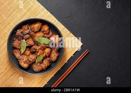 Adobo Pork in black bowl at dark slate background. Pork Adobo or Adobong Baboy is filipino cuisine dish with braised pork belly, bay leaves, soy sauce Stock Photo