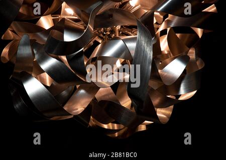 Silver and copper metal curved ribbon chandelier closeup. Modern metal lampshade. Black and golden abstract textured background. Abstract pattern Stock Photo