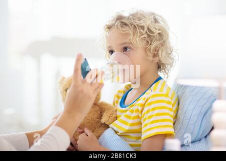 Sick little boy with asthma medicine. Mother with ill child lying in bed. Unwell kid with chamber inhaler for cough treatment. Flu season. Parent in b Stock Photo