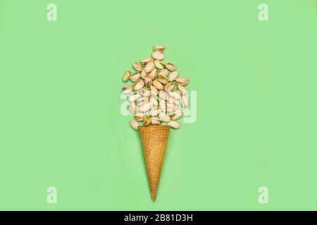 Unpeeled green pistachios with a waffle cone on a green background Stock Photo