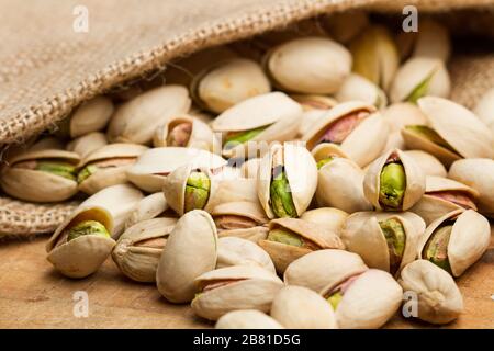 Unpeeled green pistachios in a burlap sack and on a wooden table Stock Photo