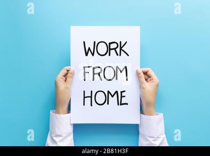 work from home concept. woman hand holding paper with word work from home isolated on blue background, studio shot. Stock Photo