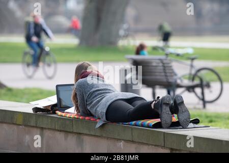 Dresden, Germany. 19th Mar, 2020. A woman lies on a wall on the banks of the Elbe and works on a laptop. On 20 March 2020 is the calendrical beginning of spring. Credit: Sebastian Kahnert/dpa-Zentralbild/ZB/dpa/Alamy Live News Stock Photo