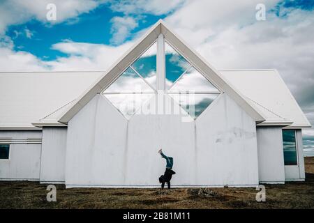 Young man doing a handstand in front of traditional wooden white house and blue cloudy sky in Iceland Stock Photo