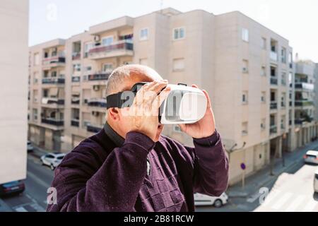 closeup of a senior caucasian man using a virtual reality headset outdoors, in front of an apartment building in a quiet city Stock Photo