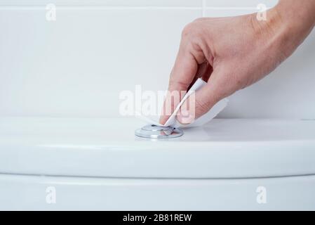 closeup of a caucasian man pressing the flush button of a toilet covering his fingers with a piece of toilet paper Stock Photo