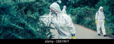 People in bacteriological protection suits looking for samples on empty road Stock Photo