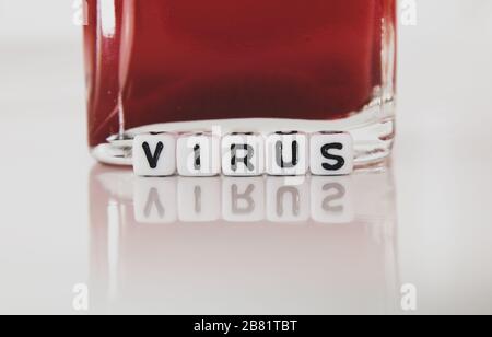 Virus white square plastic letters macro on reflective plate with red liquid in container. Macro photography. Stock Photo