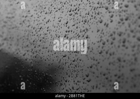 Drops of water on a car glass. Black tinted car window with raindrops, reflection of the clear sky. Texture for design. Stock Photo