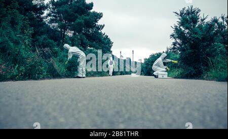 People in bacteriological protection suits looking for samples on empty road Stock Photo