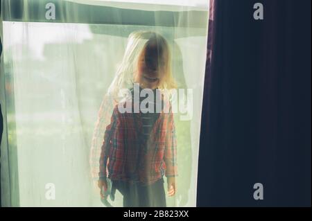 A little preschooler is standing behind a see through curtain Stock Photo