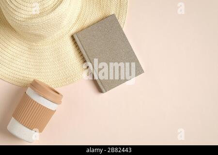 Cozy home office desk concept. Feminine table with reusable bamboo coffee cup, stylish paper notepad and straw hat on beige background. Flat lay, top Stock Photo
