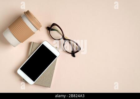Flat lay feminine home office workspace with paper notepad, glasses, reusable bamboo coffee cup, phone with blank screen mockup. Cozy female office de Stock Photo