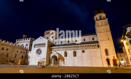 Trento 2019. Night view, in long exposure, of tourists and passersby crossing Piazza Duomo near the Triton Fountain. We are on a warm but cloudy summe Stock Photo