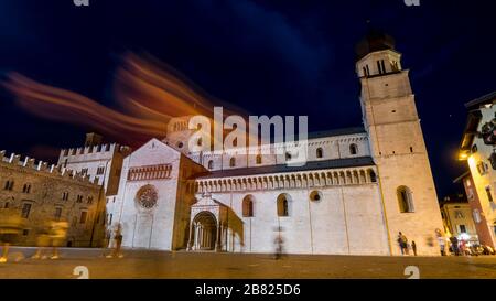 Trento 2019. Night view, in long exposure, of tourists and passersby crossing Piazza Duomo near the Triton Fountain. We are on a warm but cloudy summe Stock Photo