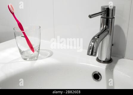 White bathroom faucet and wash basin with water glass and toothbrush