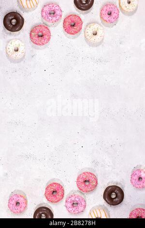 Frame of traditional doughnuts with multicolored glaze laid out top and bottom on concrete background. Top view, flat lay, copy space. Vertical orient Stock Photo