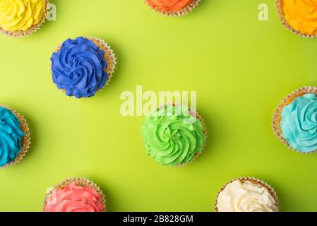 Party background with different cupcakes on bright green background. Pattern with cupcakes with colorful icing. Stock Photo