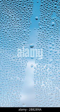 Drops water on window for mobile wallpaper design. Blue cloudy sky backdrop. Spotted abstract texture background. Spring wet weather. Droplets on glass in vertical natural cover. Fit to autumn. Stock Photo