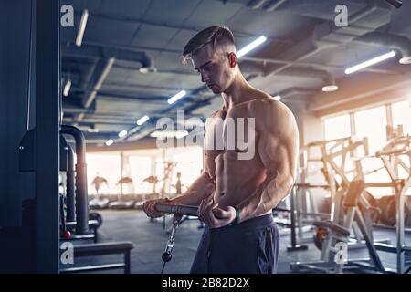 Muscular Fitness Bodybuilder Doing Heavy Weight Exercise For Biceps On Machine With Cable In The Gym. Stock Photo