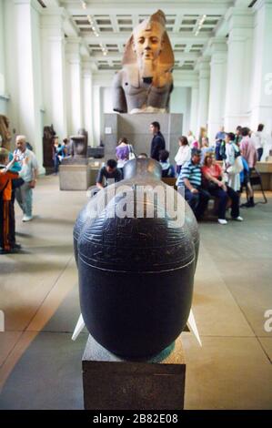 Colossal head of Egyptian Pharaoh Ramesses II, ca. 1250 B.C, British Museum, London with lots of people walking around looking at the artifacts. Sarcophagus of Merymost at the British Museum, London. 18th Dynnasty, about 1380BC from Thebes in the foreground. Stock Photo