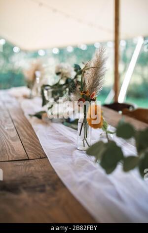 Stylish boho rustic decorations made of wood, flowers and dry wildflowers served on the festive wooden table, outdoors in tent. Stock Photo