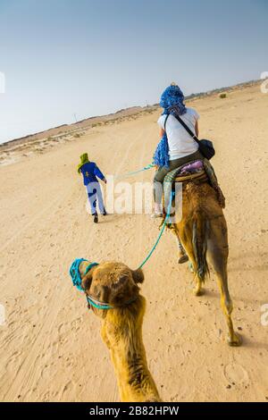 Woman and tuareg guide in a dromedary ride in the desert. Stock Photo