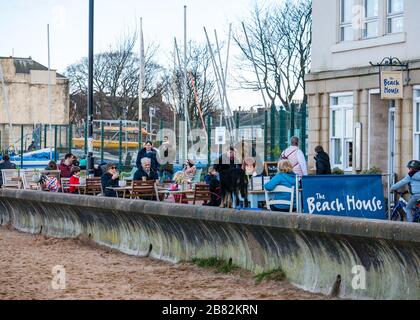 Portobello beach, Edinburgh, Scotland, United Kingdom. 19th March 2020. On a sunny Spring day, people are out enjoying the seaside. People sitting at the Beach House cafe pavement tables  during the Covid-19 Coronavirus pandemic Stock Photo