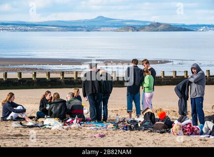 Portobello beach, Edinburgh, Scotland, United Kingdom. 19th March 2020. On a sunny Spring day, people are out enjoying the seaside. A group of young people gather to party on the beach despite advice to maintain social distance during the Covid-19 Coronavirus pandemic Stock Photo