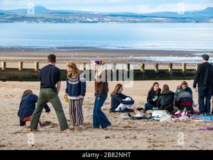 Portobello beach, Edinburgh, Scotland, United Kingdom. 19th March 2020. On a sunny Spring day, people are out enjoying the seaside. A group of young people gather to party on the beach despite advice to maintain social distance during the Covid-19 Coronavirus pandemic Stock Photo