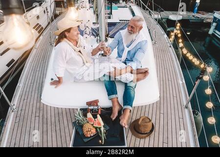 Senior couple toasting champagne on sailboat vacation - Happy mature people having fun celebrating wedding anniversary on boat trip Stock Photo