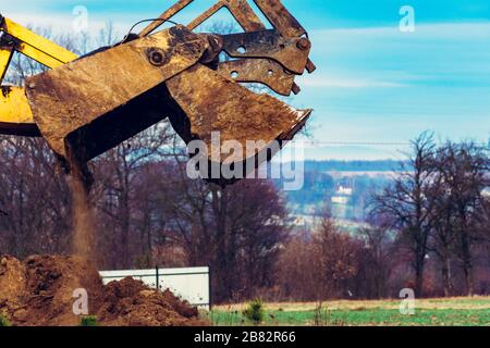 A close-up excavator loads soil into the bucket for further road installation. Stock Photo