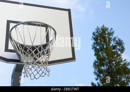 basketball backboard with a basket on a blue sky and green tree background, concept of sports, active lifestyle and outdoor recreation Stock Photo