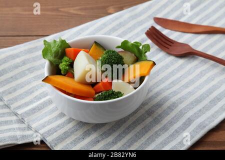 steamed vegetable salad in bowl isolated on wooden table Stock Photo