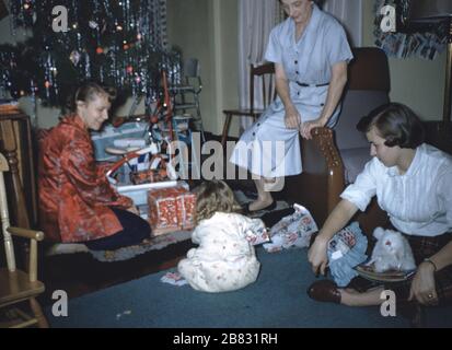 A family with children gather and open presents beside a Christmas tree on christmas morning, 1965. () Stock Photo
