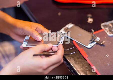 A man is repairing a mobile phone. In the frame, his hands and details of the device. repair shop for gadgets Stock Photo