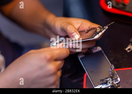 A man is repairing a mobile phone. In the frame, his hands and details of the device. repair shop for gadgets Stock Photo