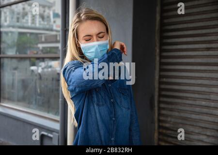 Caucasian woman wearing a covid19 coronavirus mask outside and coughing