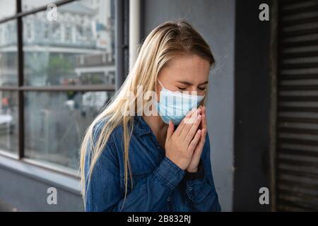 Caucasian woman wearing a covid19 coronavirus mask outside and coughing Stock Photo