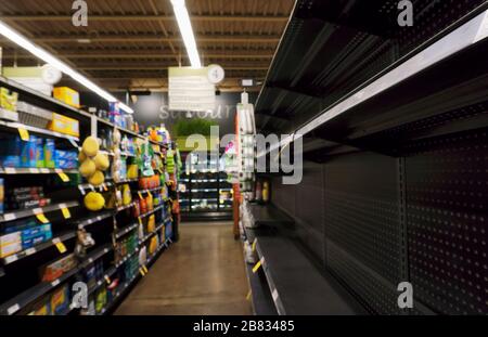 Partially empty supermarket shelves due to panic buying and hoarding of shortage of toilet paper, paper towel, napkins and cleaning products, as result of pandemic outbreak of novel coronavirus in Toronto, Ontario, Canada on March 19, 2020. Narrow focal point on the edge of the right shelf to blur the details of the products
