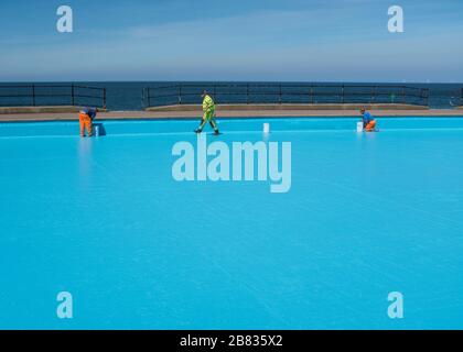Workmen painting a paddling pool blue on the seafront at Llandudno, Conwy, Wales. Stock Photo