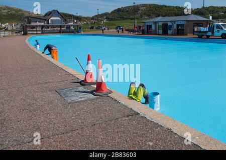 Workmen painting a paddling pool blue on the seafront at Llandudno, Conwy, Wales. Stock Photo