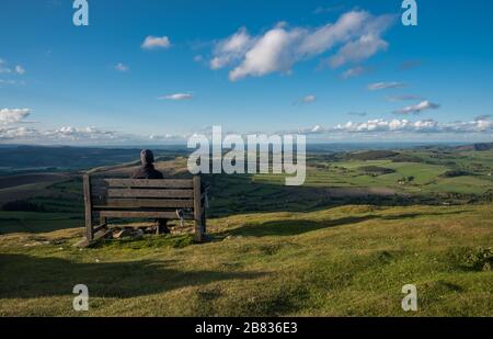 A hiker sits on a bench looking out over the Mid Wales Countryside. Corndon Hill, Powys, Wales. Stock Photo