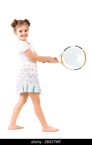 Small positive girl in stylish clothing standing and holding tennis racket in hand and smiling over white background. Active healthy lifestyle, hobbie Stock Photo