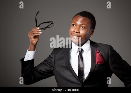 Young handsome african businessman in grey costume, white shirt, tie and glasses standing over grey background. Trendy business look and outfit for me Stock Photo