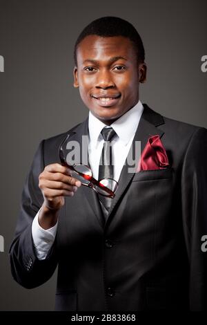 Young handsome african businessman in grey costume, white shirt, tie and glasses standing over grey background. Trendy business look and outfit for me Stock Photo
