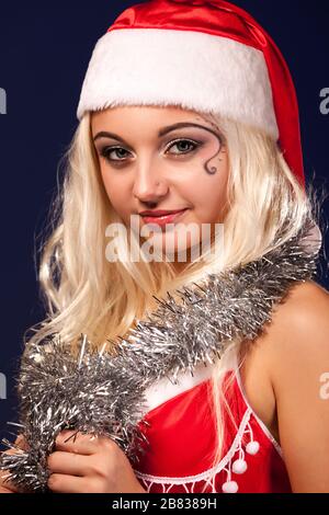 Charming young girl in a New Year's red suit with decoration posing on a blue background. The concept of gifts and wishes come true. Advertising space Stock Photo