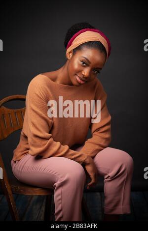 Young black woman sitting on a wooden chair looking at camera. Stock Photo