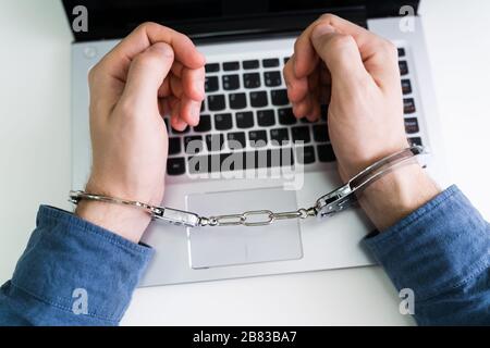 Close-up Of Person's Hand With Handcuff Using Laptop Stock Photo