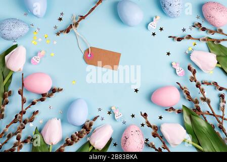 Decorative frame with Easter handcraft painted eggs, tulips flowers and paper label on a light blue background. Stock Photo
